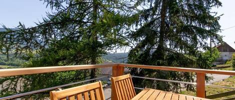 A wooden table and chairs on a balcony with a view of a large coniferous tree and a distant landscape.
