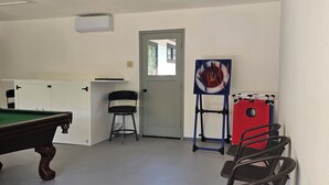 A room with a pool table, chairs, a door, and a red exercise equipment.
