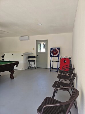 A room with a pool table, chairs, a door, and a red exercise equipment.