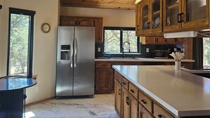 A kitchen with wooden cabinets, a stainless steel refrigerator, a marble floor, and a skylight.
