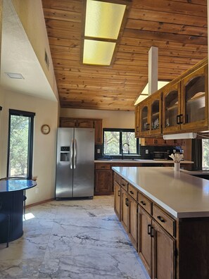 A kitchen with wooden cabinets, a stainless steel refrigerator, a marble floor, and a skylight.