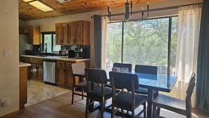 A kitchen with wooden cabinets, a dining table with chairs, and a large window with curtains.