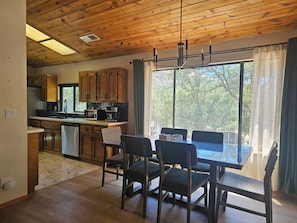 A kitchen with wooden cabinets, a dining table with chairs, and a large window with curtains.
