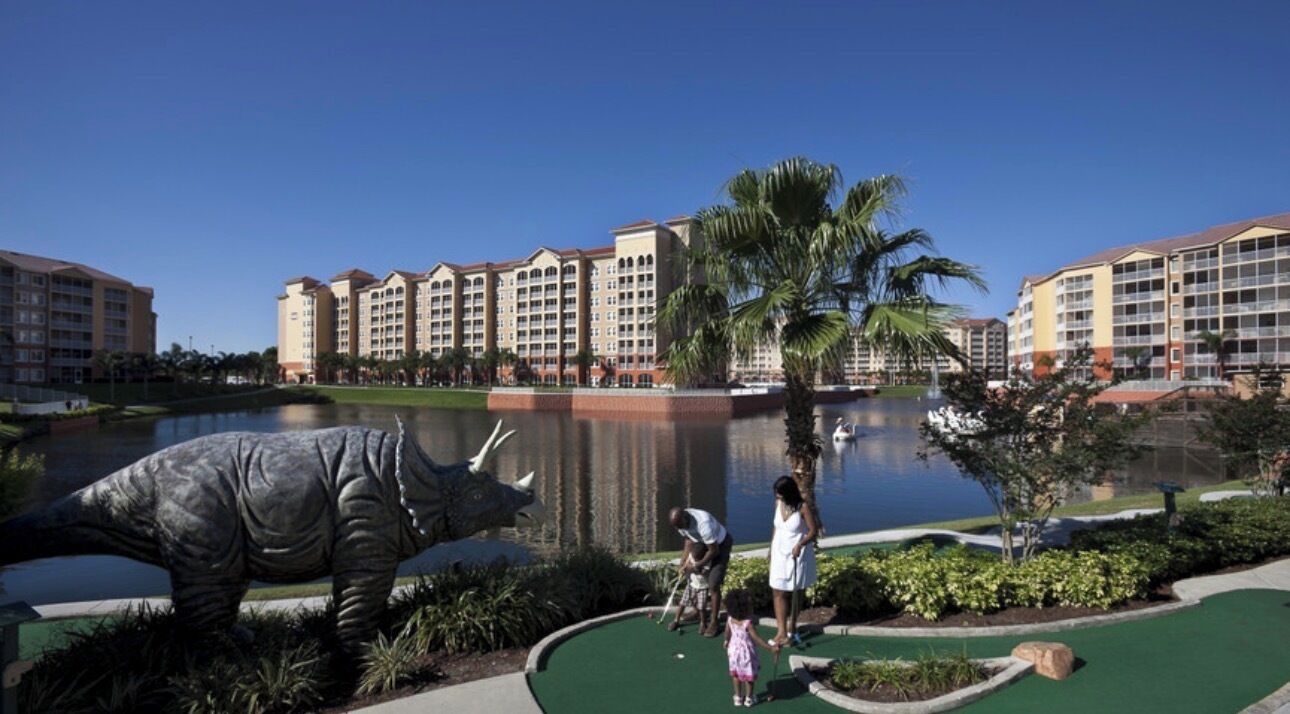 A hotel with multiple buildings, a water body, and a dinosaur statue.