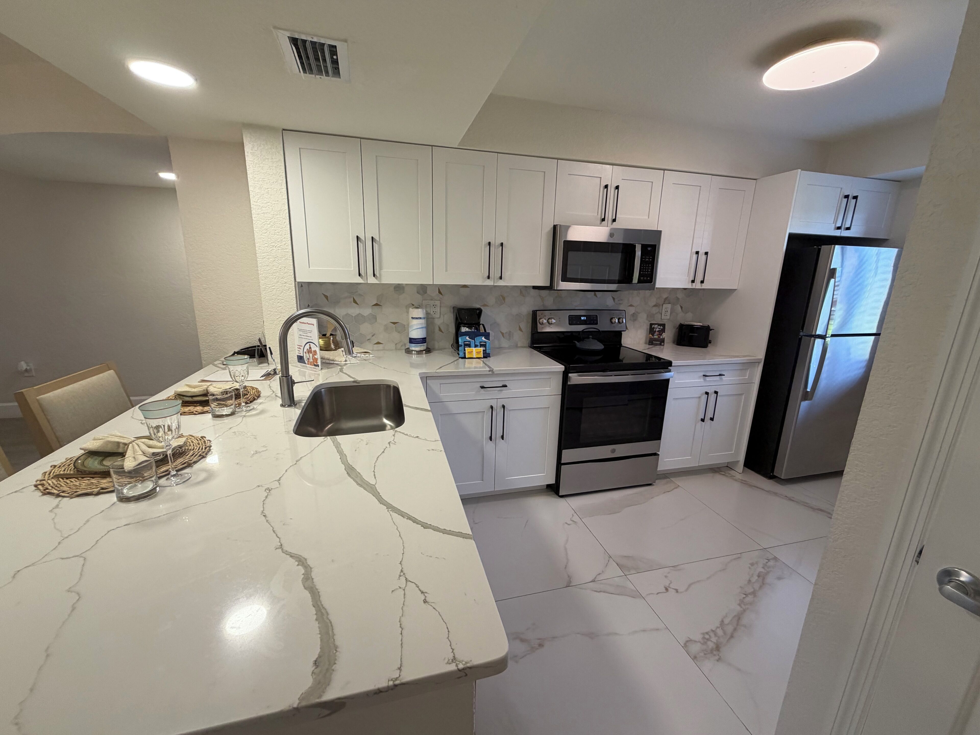 A modern kitchen with white cabinets, a stainless steel refrigerator, a microwave, and an oven.