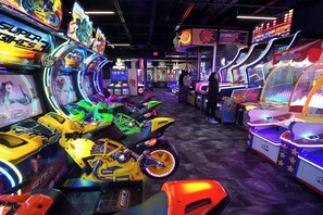 Een overdekte speelhal met diverse spelautomaten, waaronder race- en basketbalspellen.