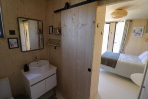 A wooden-paneled room with a bed, a white sink, and a mirror. - Delphine's Cocon Champenois (SAINT ETIENNE AU TEMPLE)