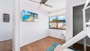 Ein Zimmer mit Deckenventilator, einem Strandbild, einem Fenster mit Aussicht und einem weißen Bett mit blauem Teppich.