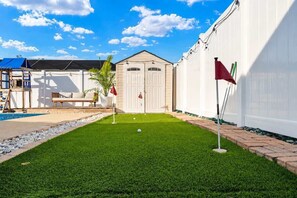 A well-maintained lawn with a small pool, a covered seating area, and a white building with a garage. - Heated Pool House Near Beach w/Game Room & Theater (Pinellas Park)