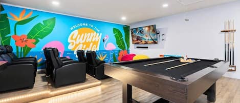 Uma mesa de bilhar com suporte para tacos, um sofá e uma parede com um mural colorido.