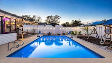 Une piscine à l’eau d’un bleu cristallin, entourée d’une terrasse aménagée avec des meubles d’extérieur et illuminée de guirlandes lumineuses.