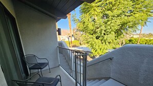 A balcony with a chair, a small table, and a view of a tree and distant landscape.