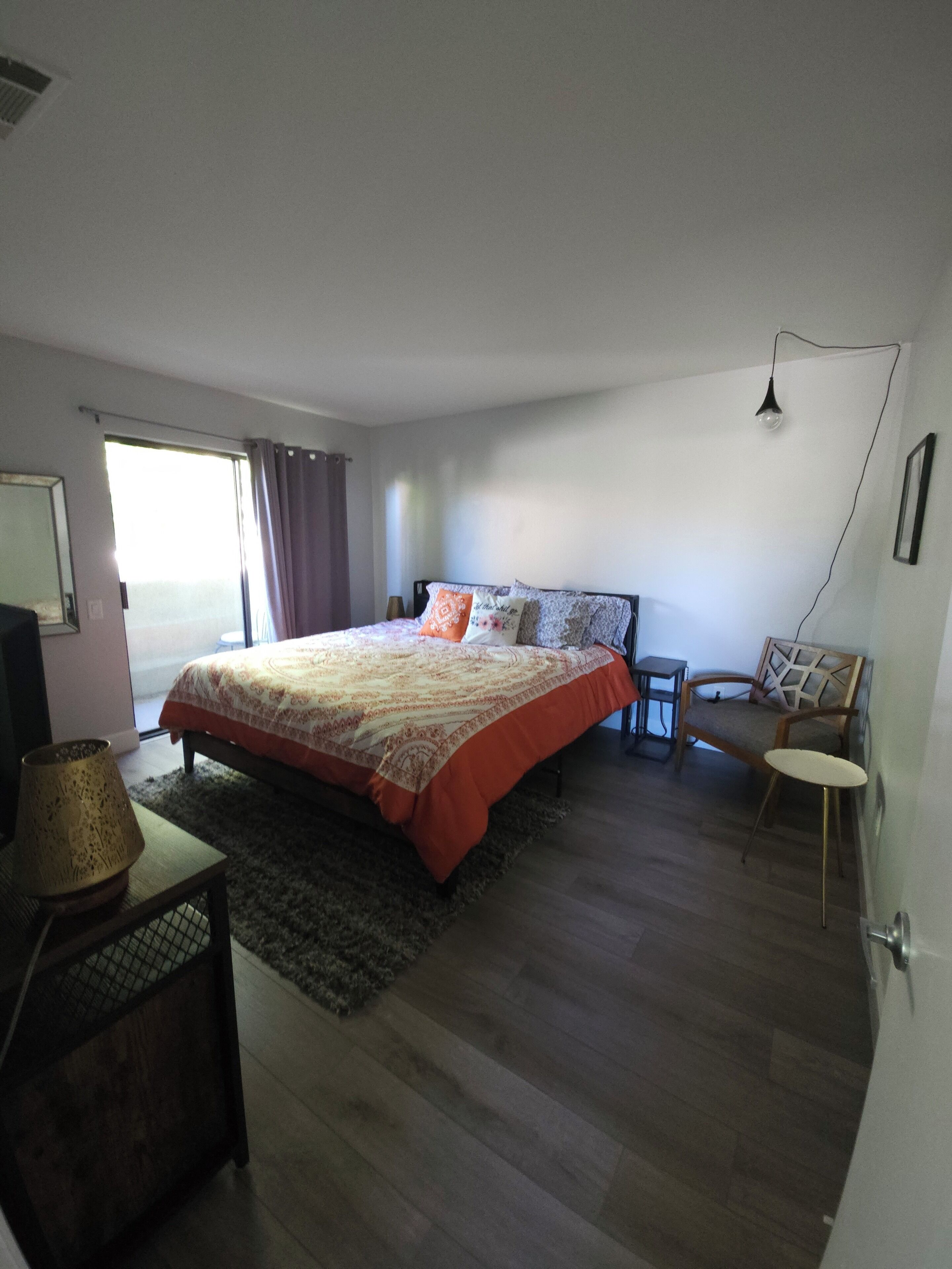 Une chambre à coucher avec un lit, une chaise, une petite table et une lampe.