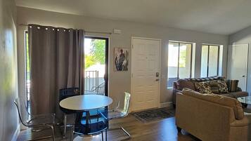 A living room with a ceiling fan, a dining table with chairs, a sofa, and a door.