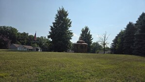 A grassy field with a gazebo and a flagpole.