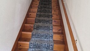 A wooden staircase with a patterned carpet, flanked by walls with framed pictures.
