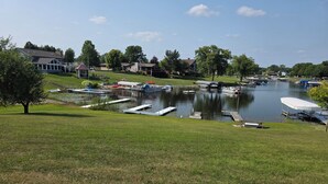 A lakeside view with boats docked, grassy areas, and houses in the background.