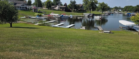 A lakeside view with boats docked, grassy areas, and houses in the background.