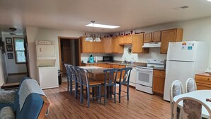 A compact kitchen with wooden cabinets, a central island with chairs, a white refrigerator, and a microwave.