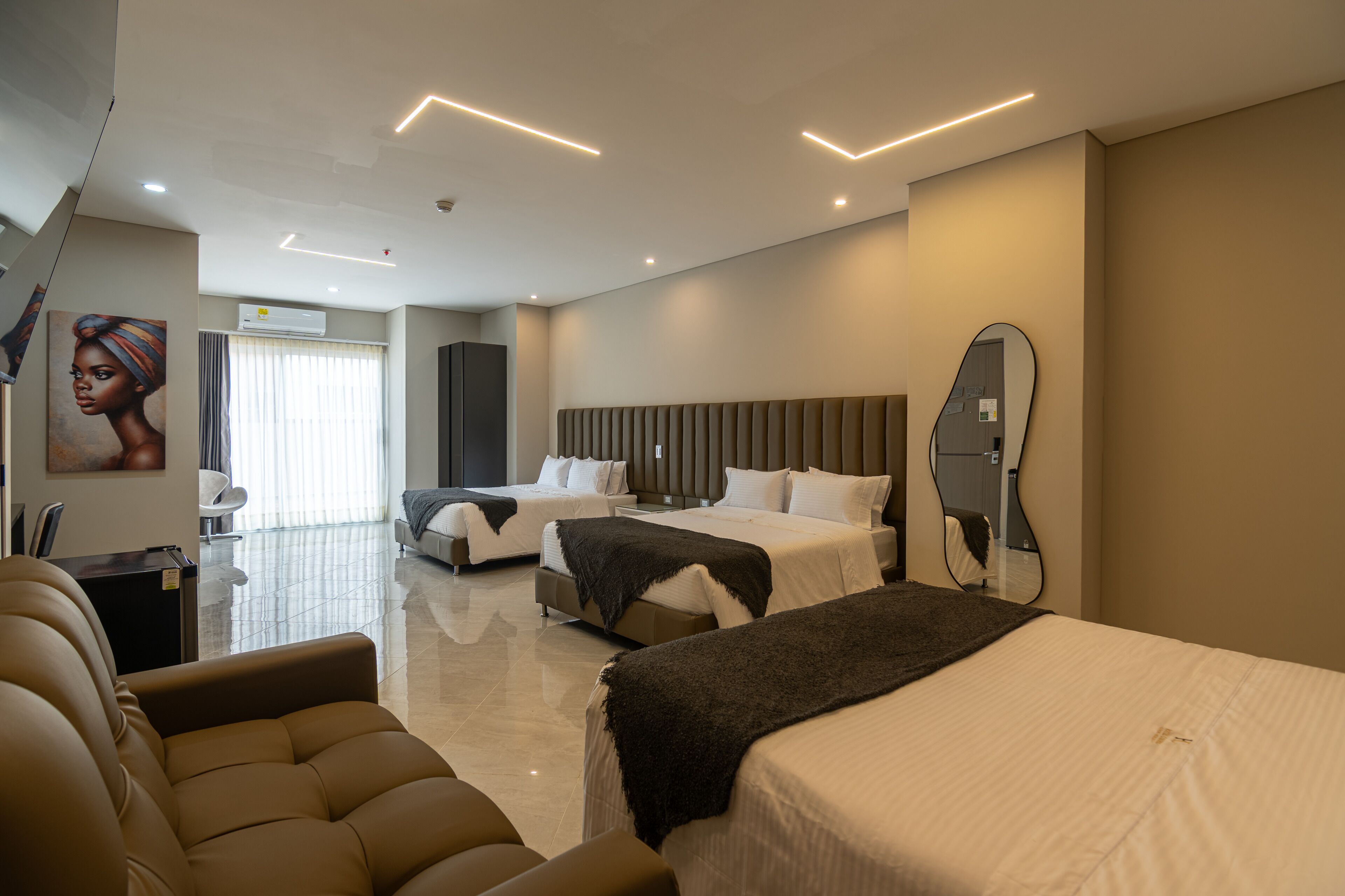 Quarto de hotel moderno com uma cama grande, uma cama menor, um sofá, uma escrivaninha e um espelho.