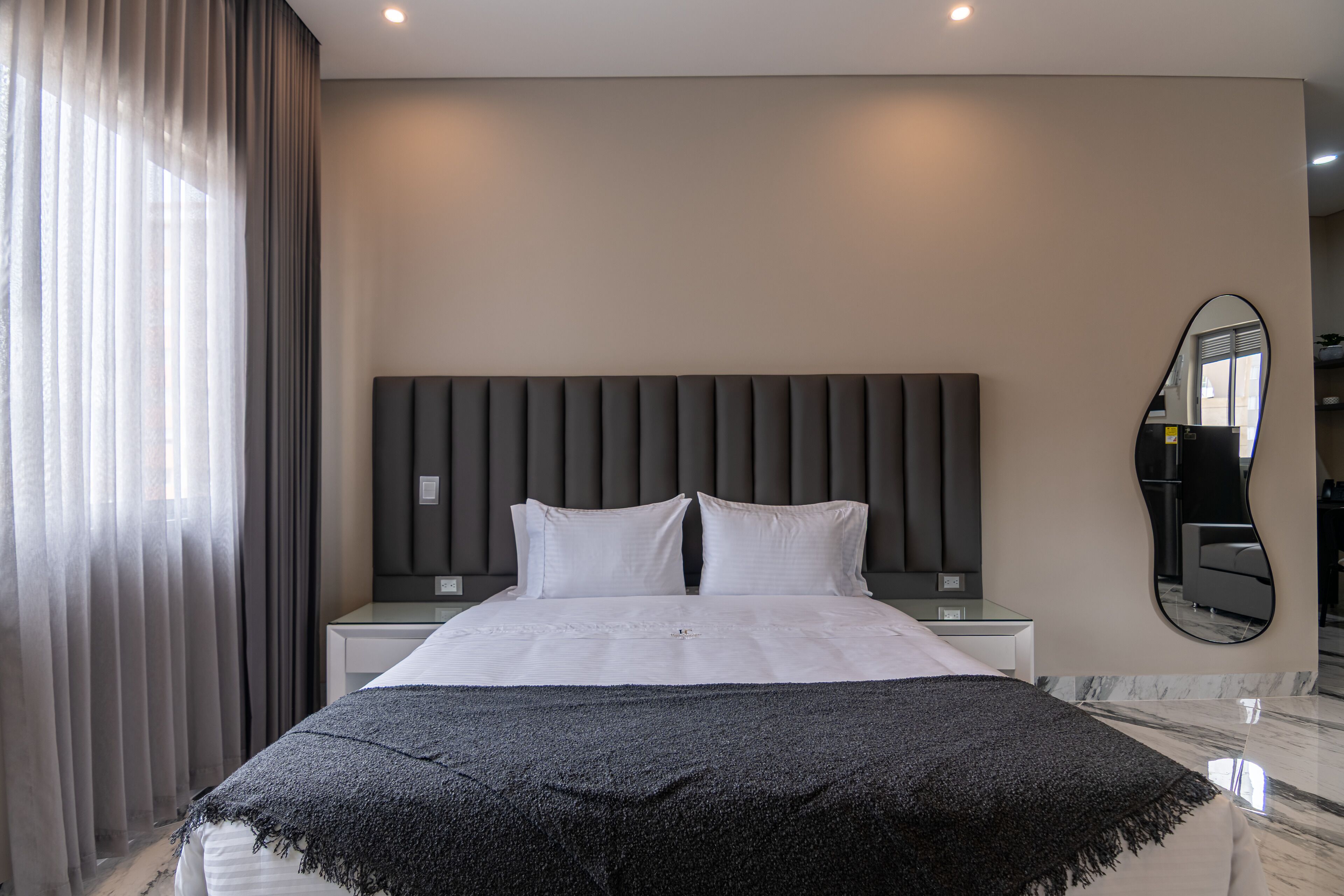 A hotel room with a bed, a bedside table, a mirror, and a view of the hallway.