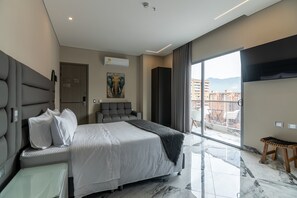 Ett modernt hotellrum med en stor säng, en sittgrupp, ett stort fönster med utsikt över staden och ett konstverk som hänger på väggen.