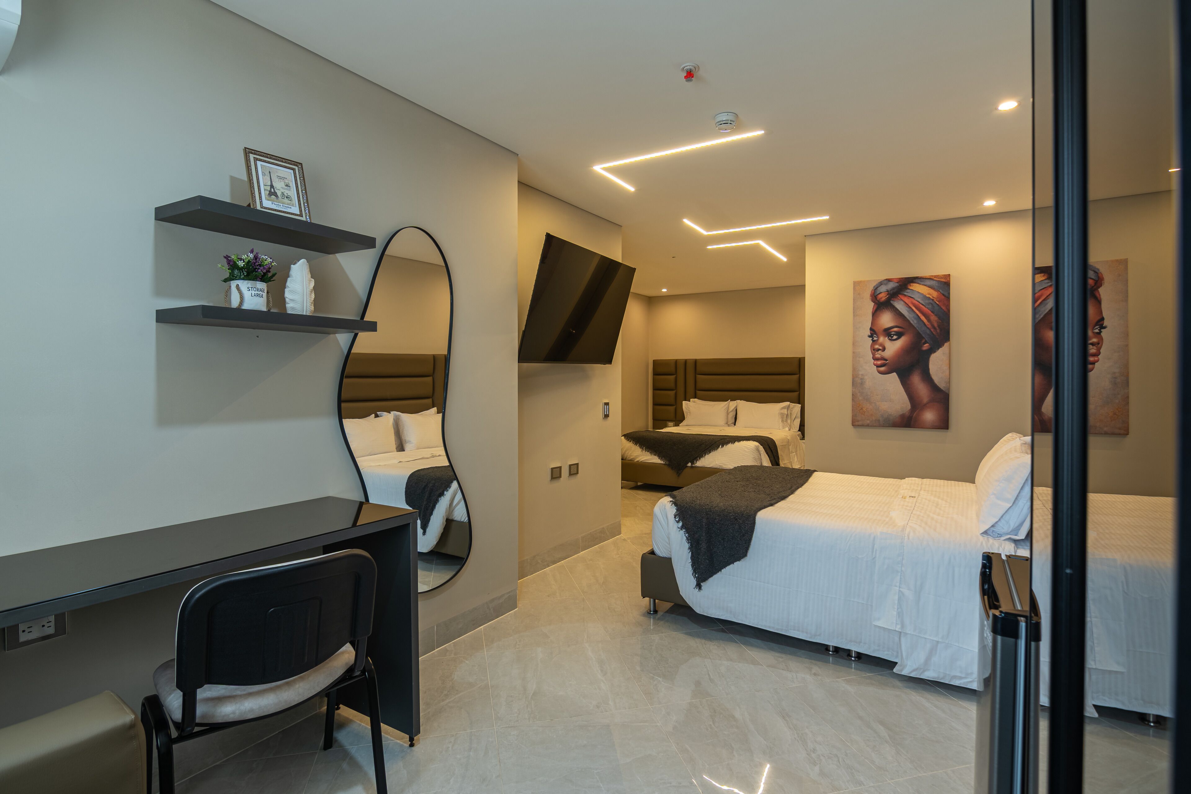 Ein modernes Hotelzimmer mit einem Bett, einem Schreibtisch, einem Stuhl, einem großen Spiegel und Kunstwerken an den Wänden.
