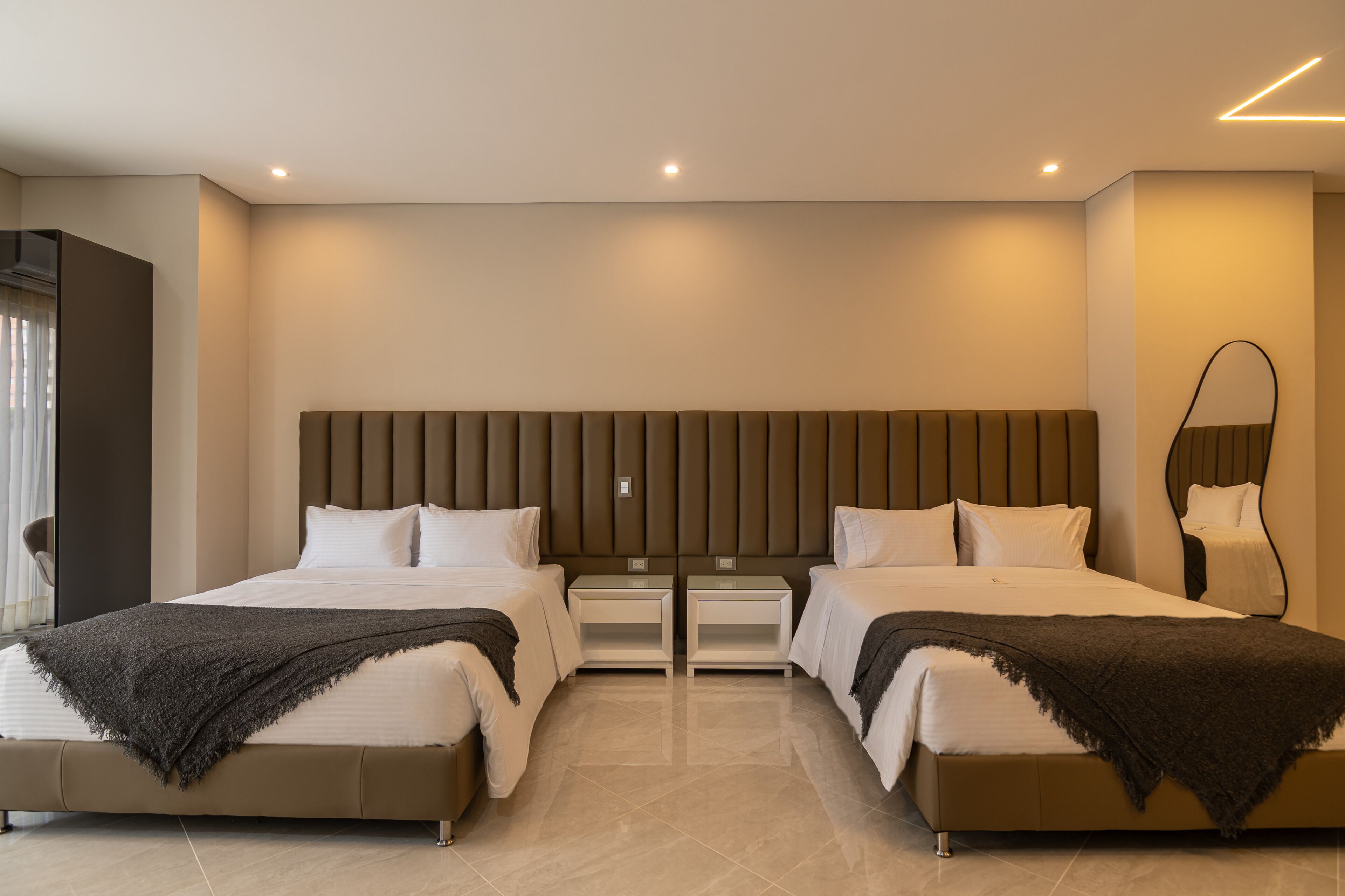 Habitación de hotel moderna con dos camas, un espejo grande y una decoración en tonos neutros.