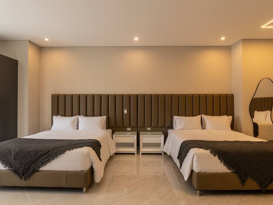 Habitación de hotel moderna con dos camas, un espejo grande y una decoración en tonos neutros.