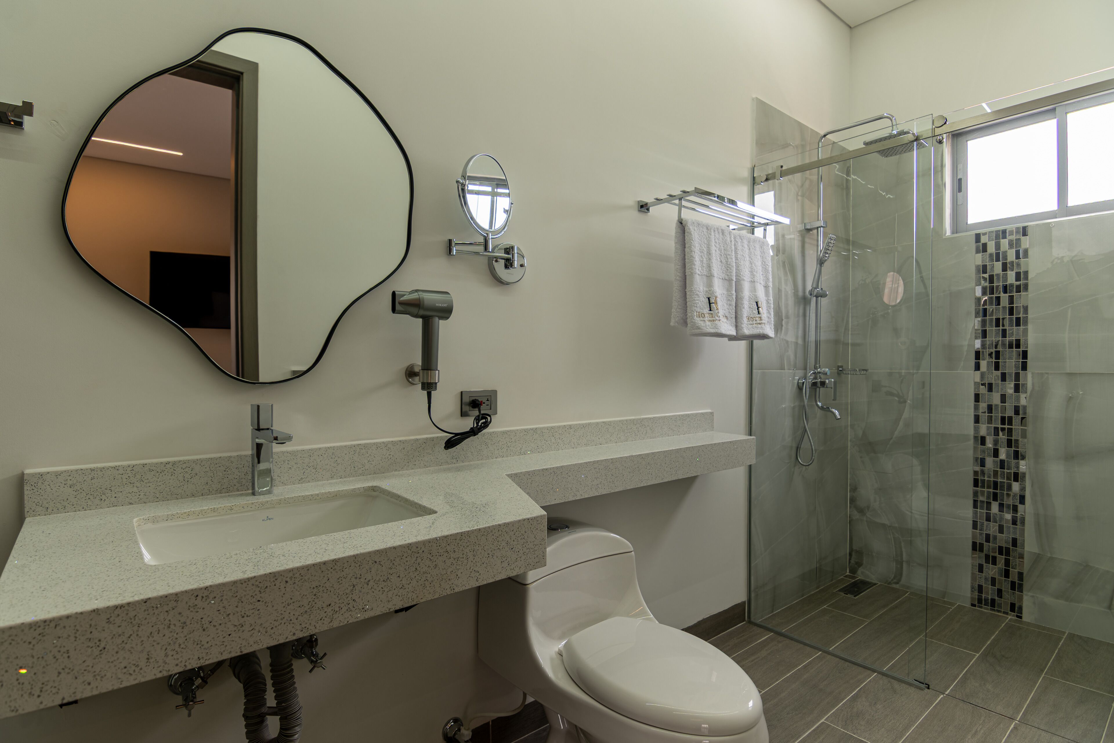A modern bathroom with a large mirror, a toilet, a shower, and a vanity with a sink.