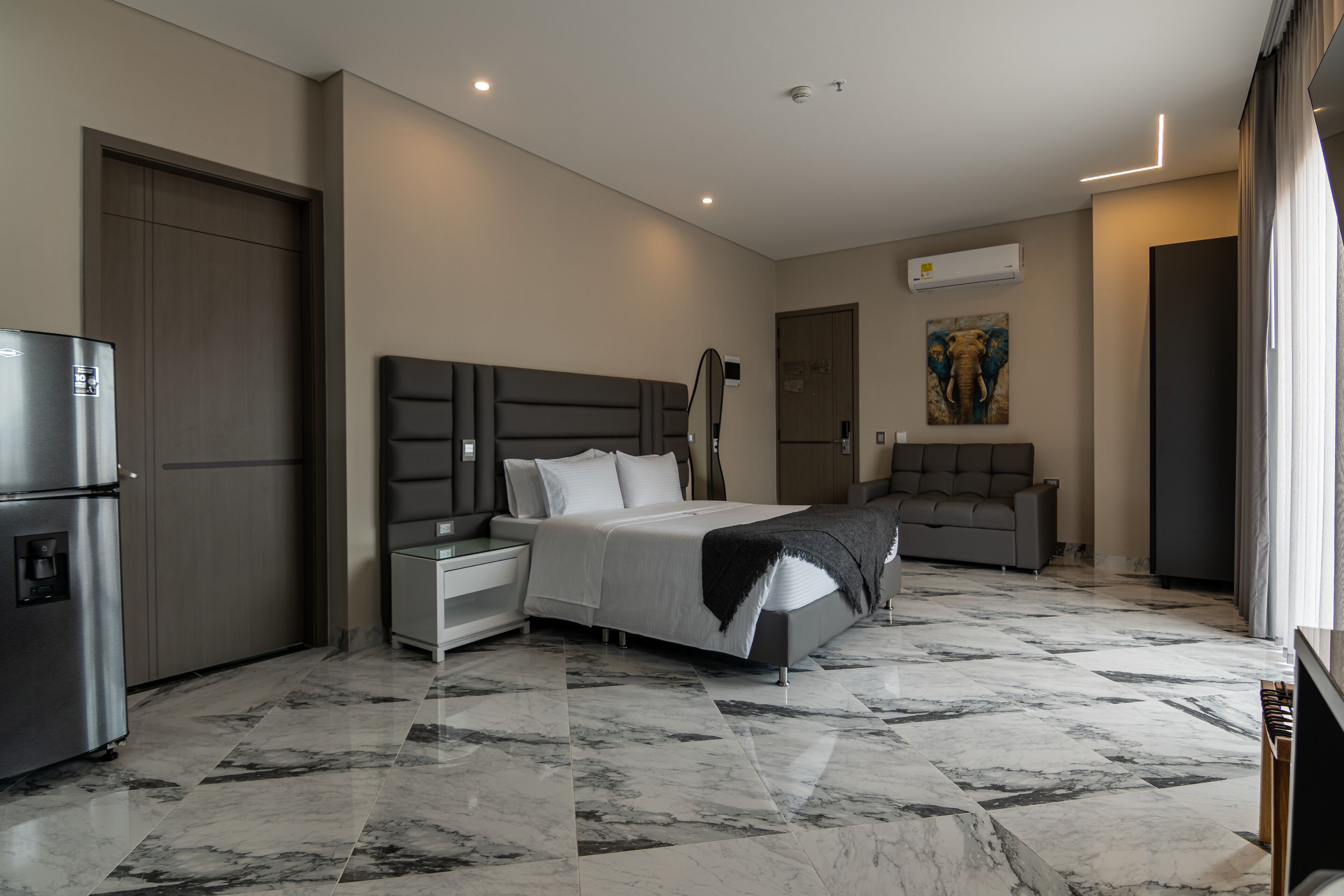 Een moderne hotelkamer met een marmeren vloer, een bed met hoofdeinde, een sofa, een koelkast en een airconditioner.