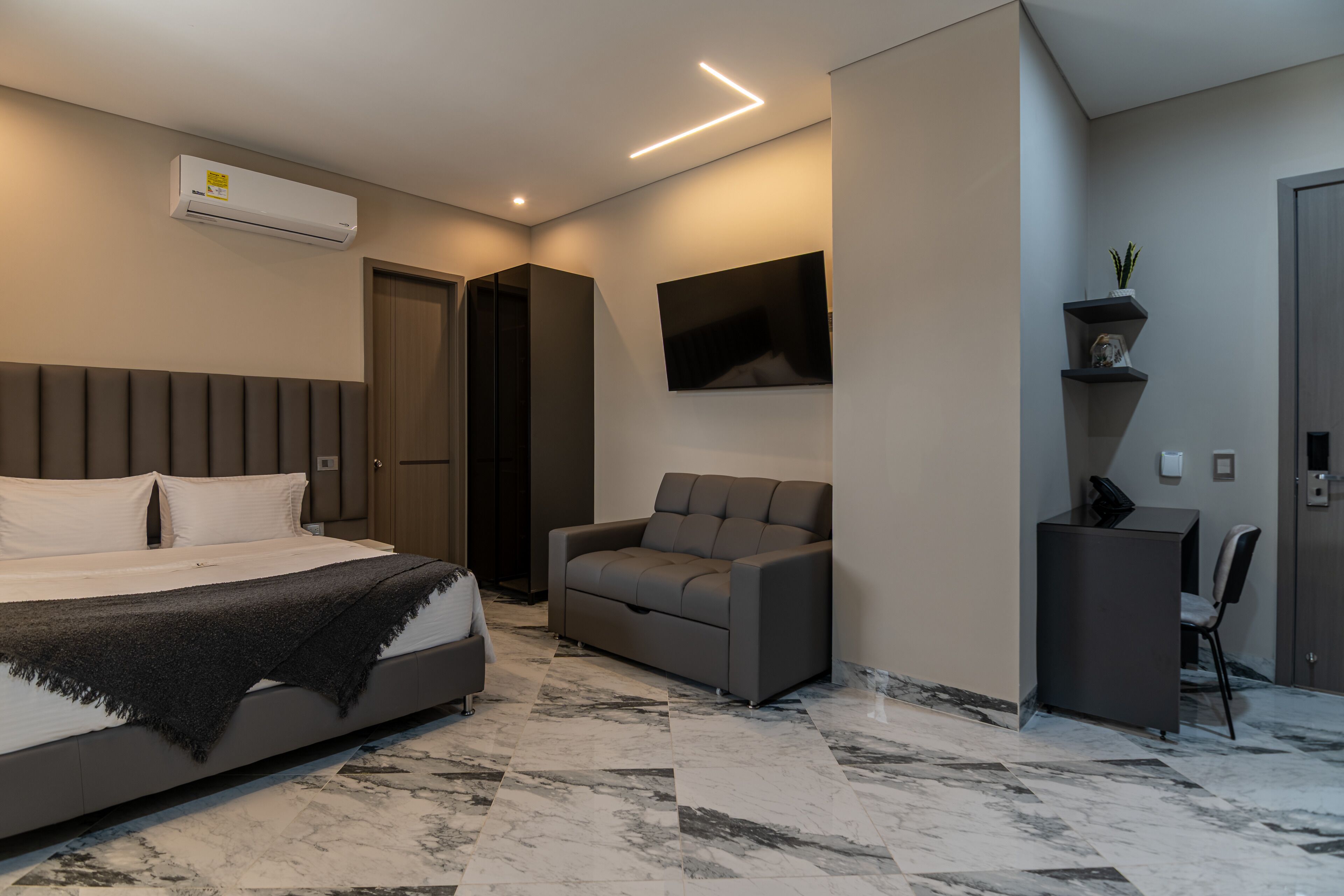 A modern bedroom with a bed, a sofa, a TV, and a desk.