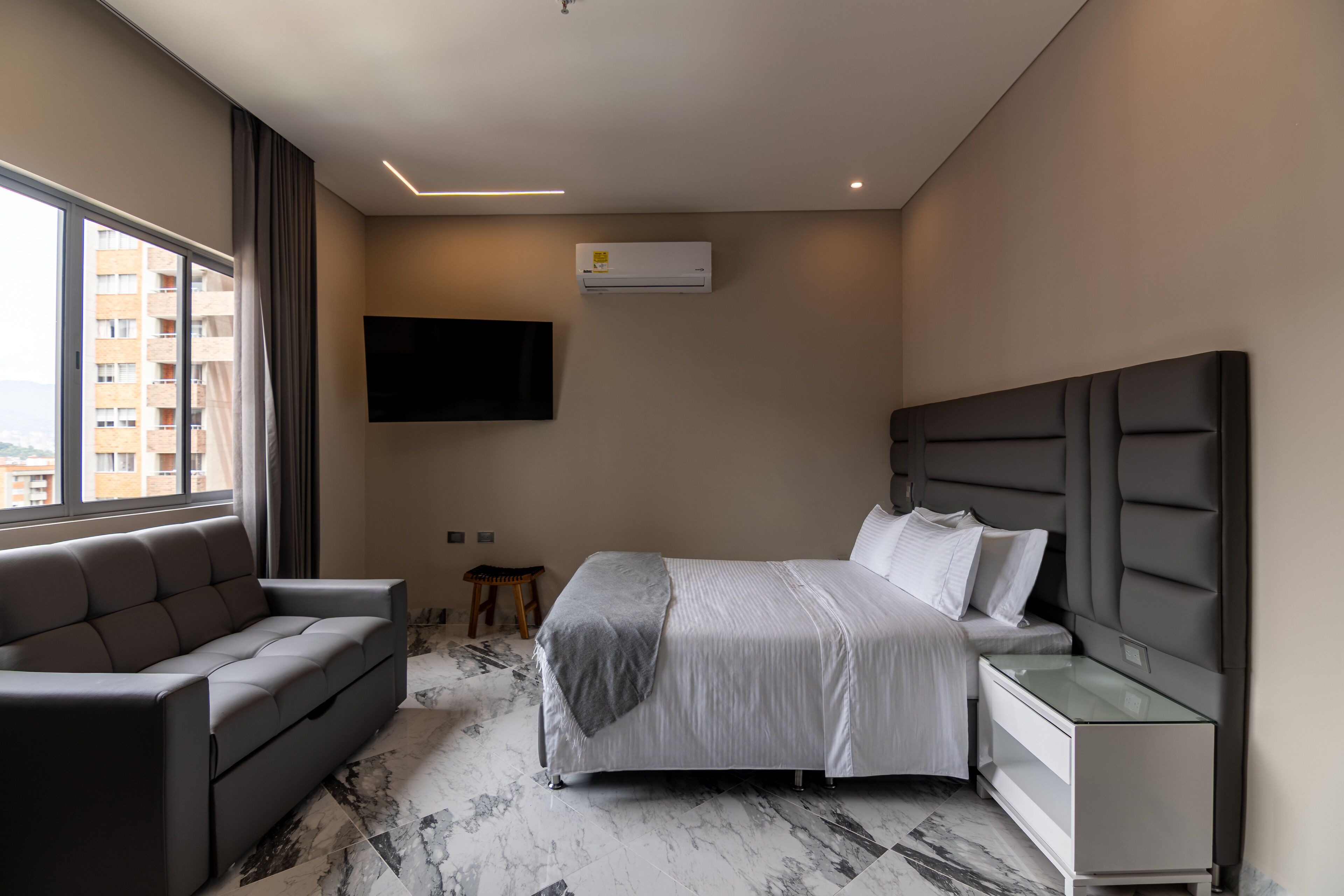 A modern hotel room with a bed, a sofa, a TV, and a desk.
