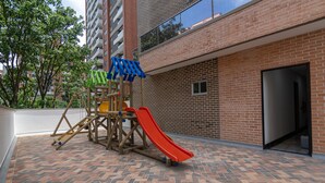 Ein Kinderspielbereich mit Rutsche und Klettergerüsten, neben einem Backsteinhaus mit Glastür.