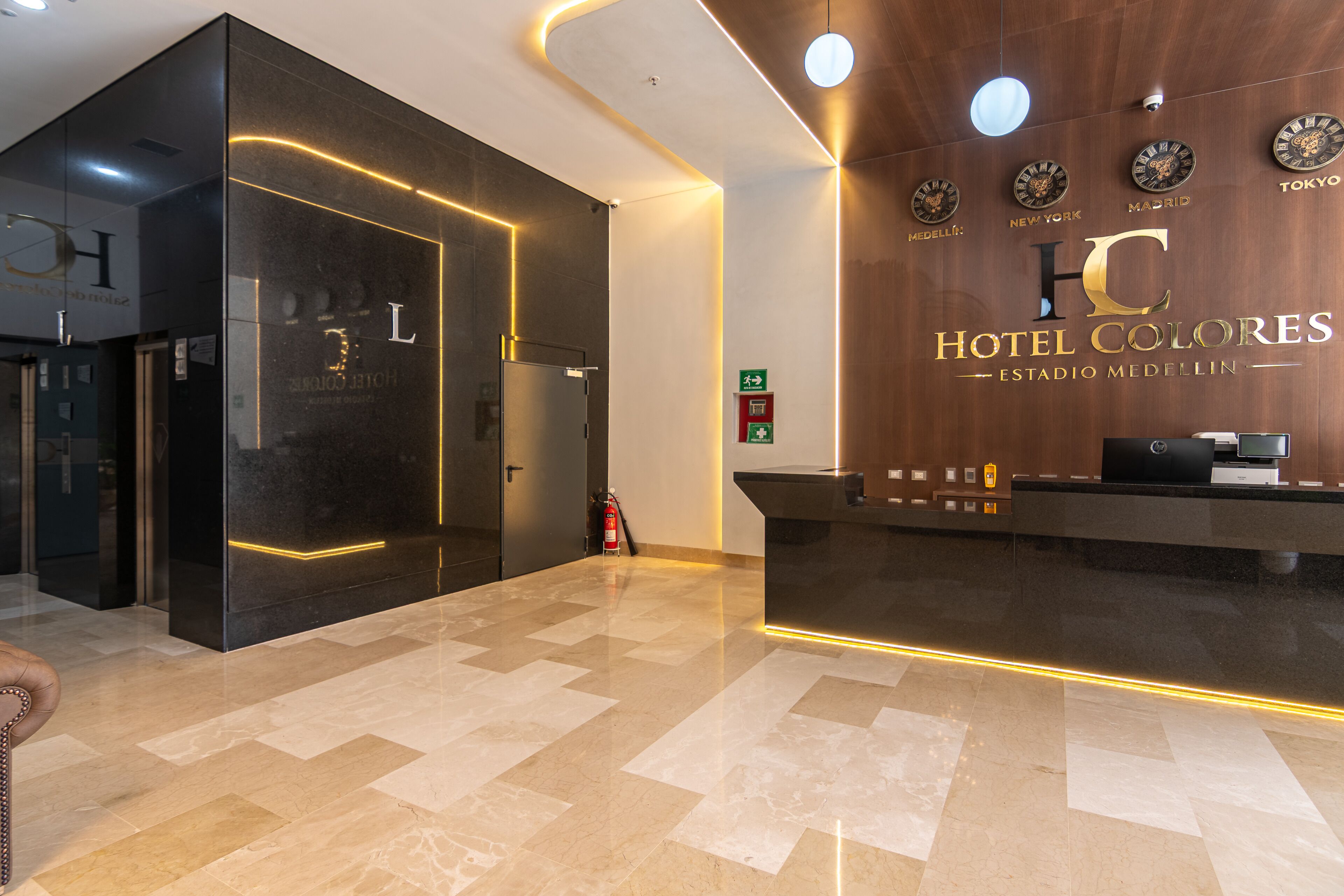 Un hall de hotel con una mesa de recepción, un extintor y una pared con relojes.