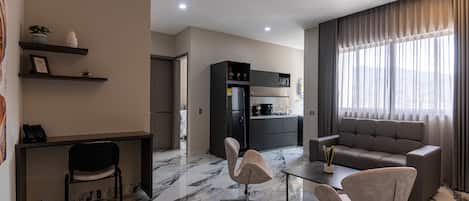 A modern living room with a sofa, two chairs, a coffee table, and a kitchen area with cabinets and appliances.