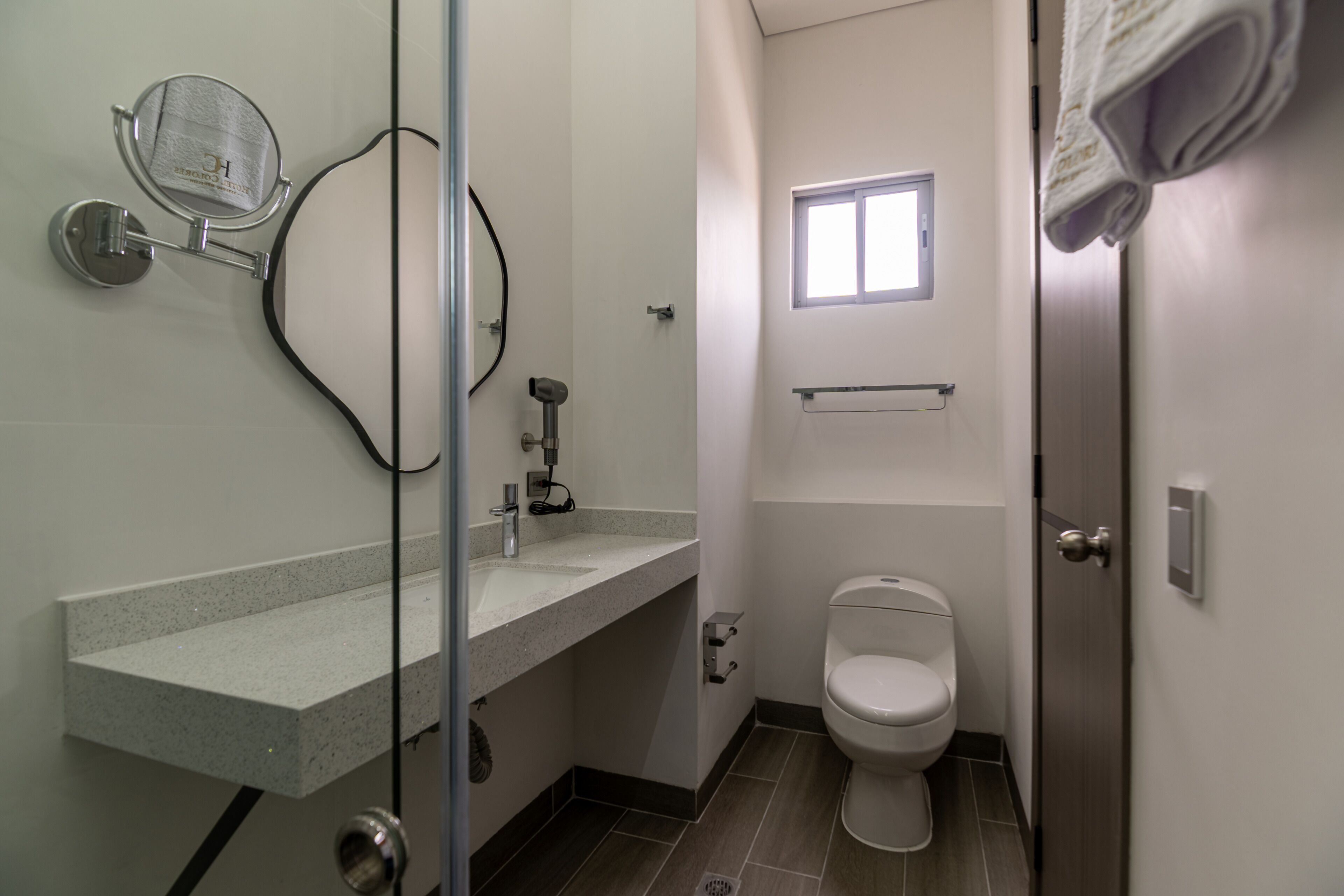 Un baño con cabina de ducha de vidrio, inodoro y lavamanos con un perchero encima.