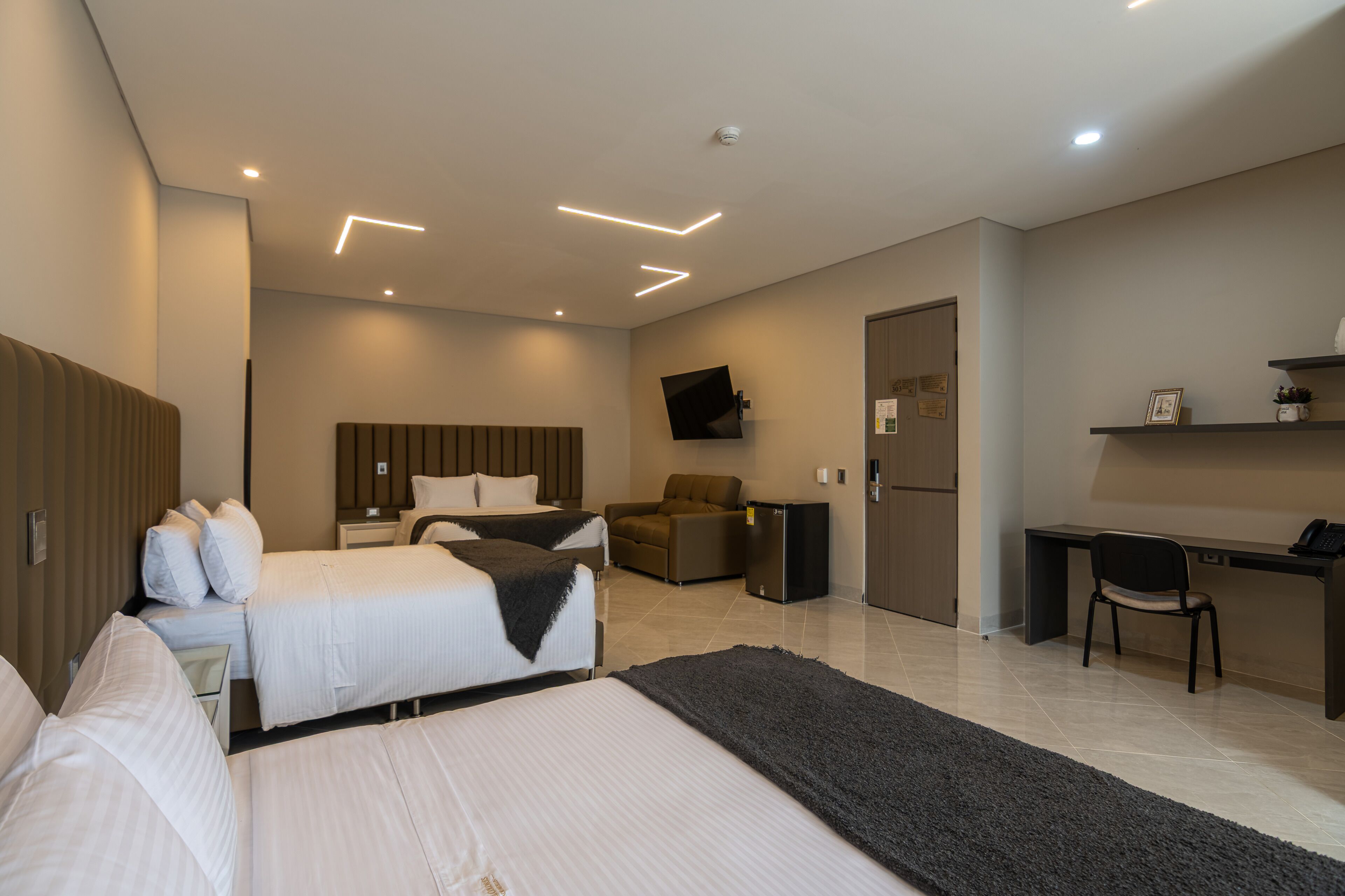 A hotel room with two beds, a desk, a chair, a TV, and a refrigerator.
