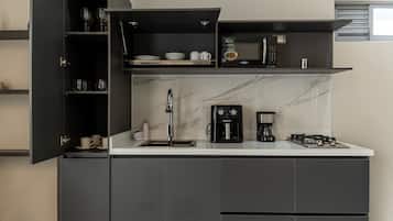 A modern kitchen with dark cabinetry, a marble countertop, a coffee maker, and a range hood.