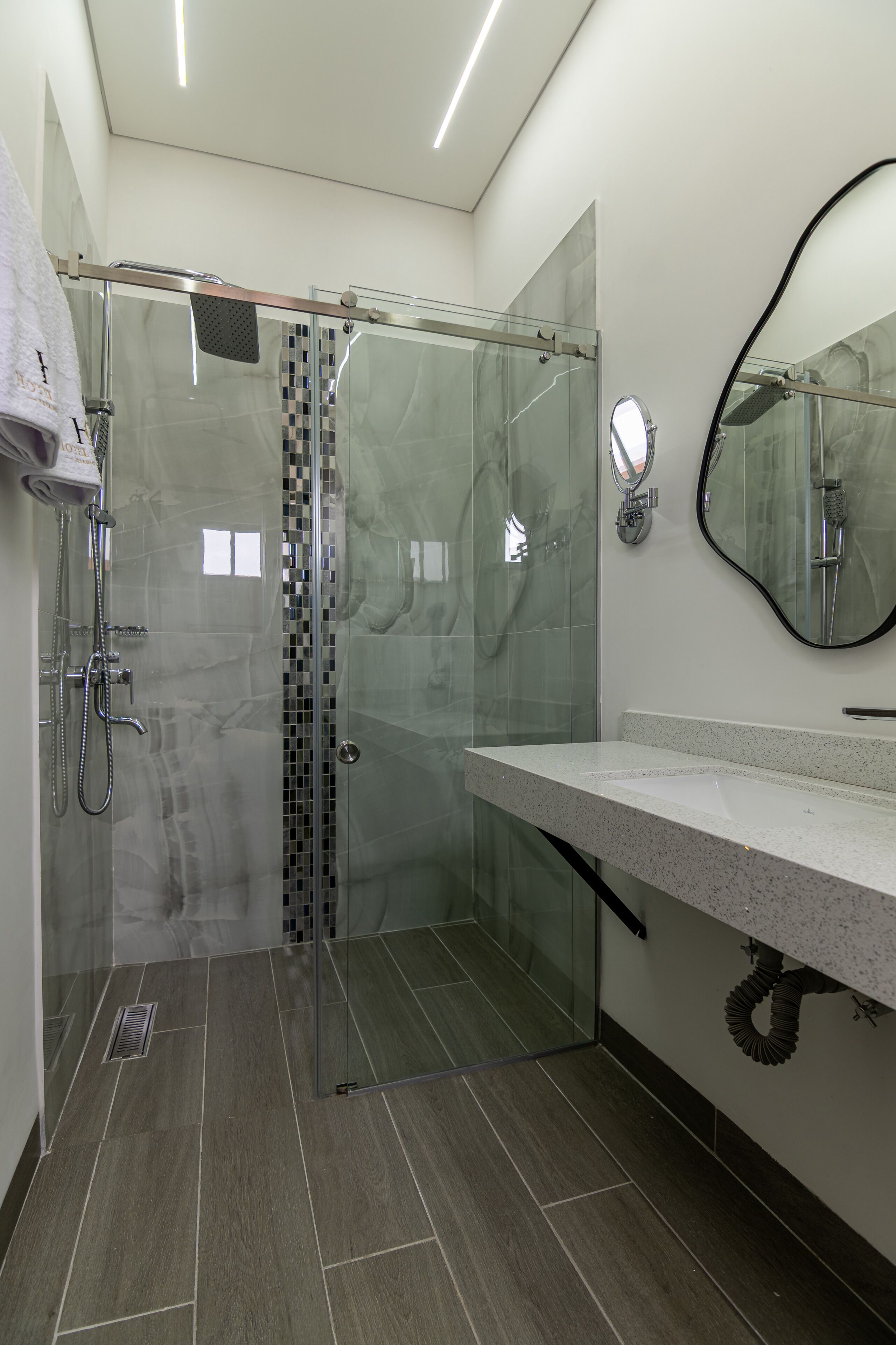 Un baño moderno con ducha envuelta en cristal, pared de azulejos de mármol y un espejo grande.