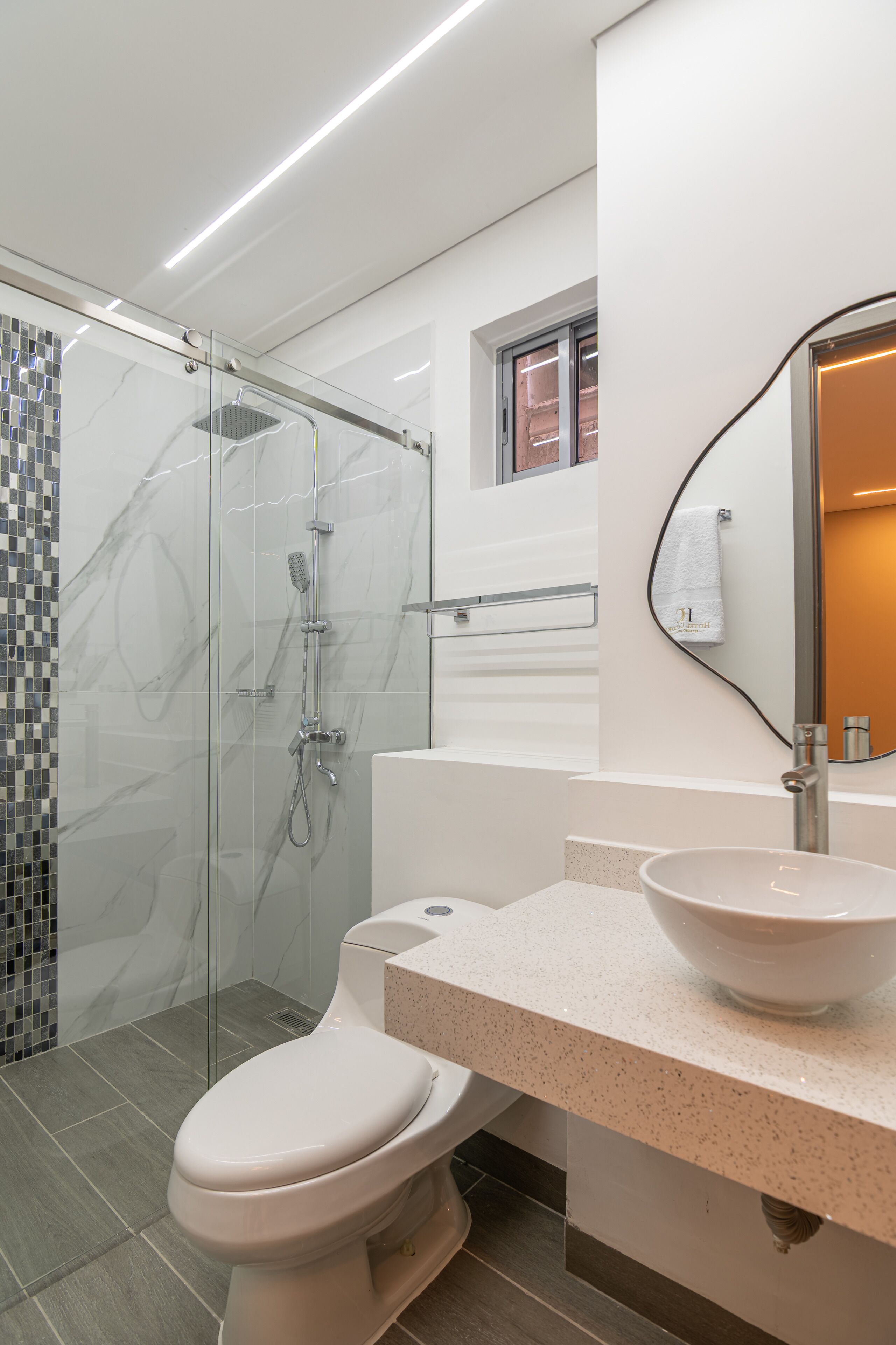Un baño moderno con ducha envuelta en vidrio, inodoro y lavamanos con espejo superior.