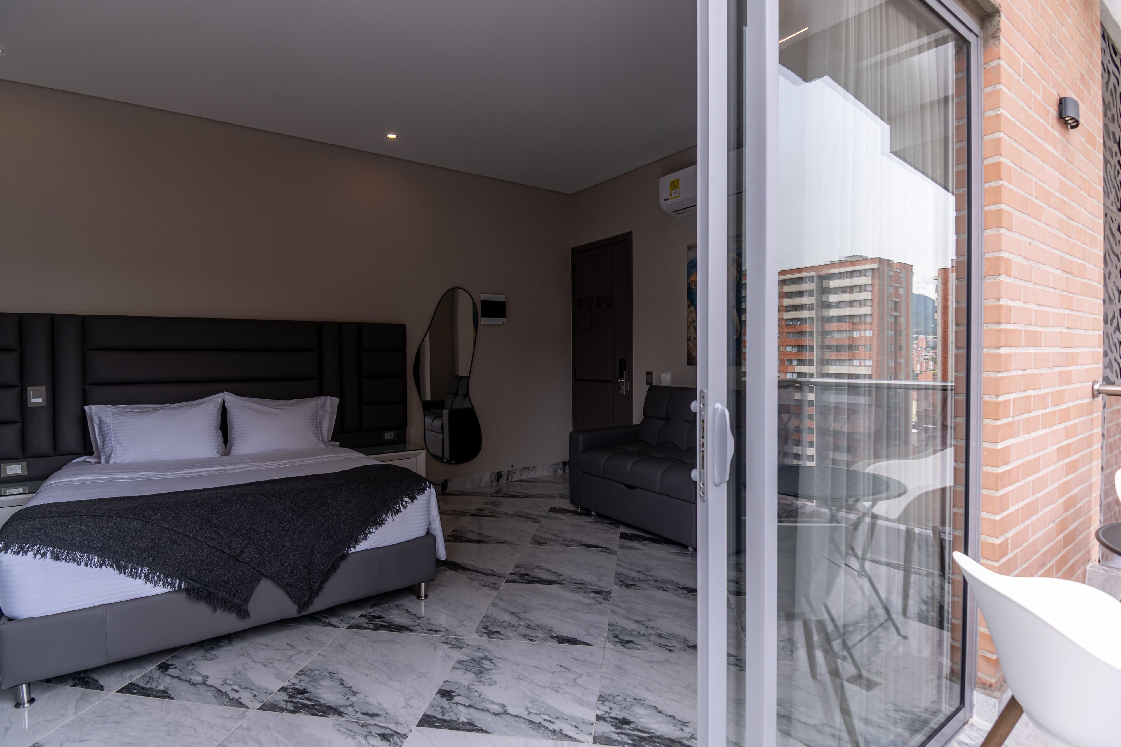 Ein modernes Hotelzimmer mit Bett, einer Sitzecke und einem Balkon mit Blick auf die Stadt.