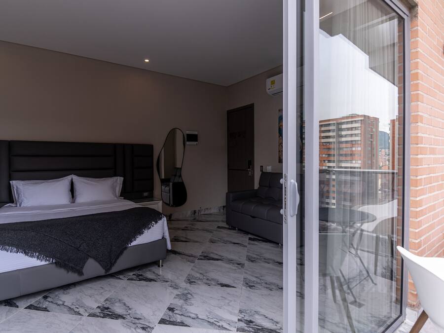 A modern hotel room with a bed, a sofa, and a balcony with a city view.