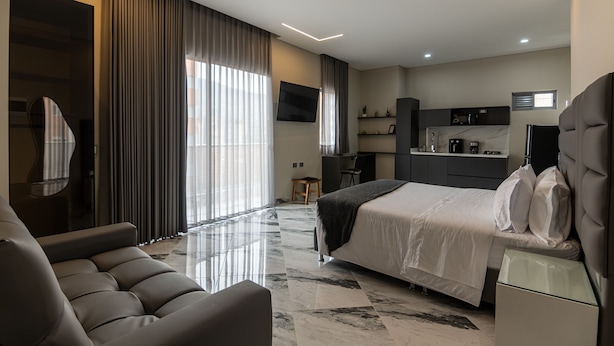 Ein modernes Hotelzimmer mit einem großen Bett, einer Sitzecke, einer Küchenzeile und einem Fernseher.