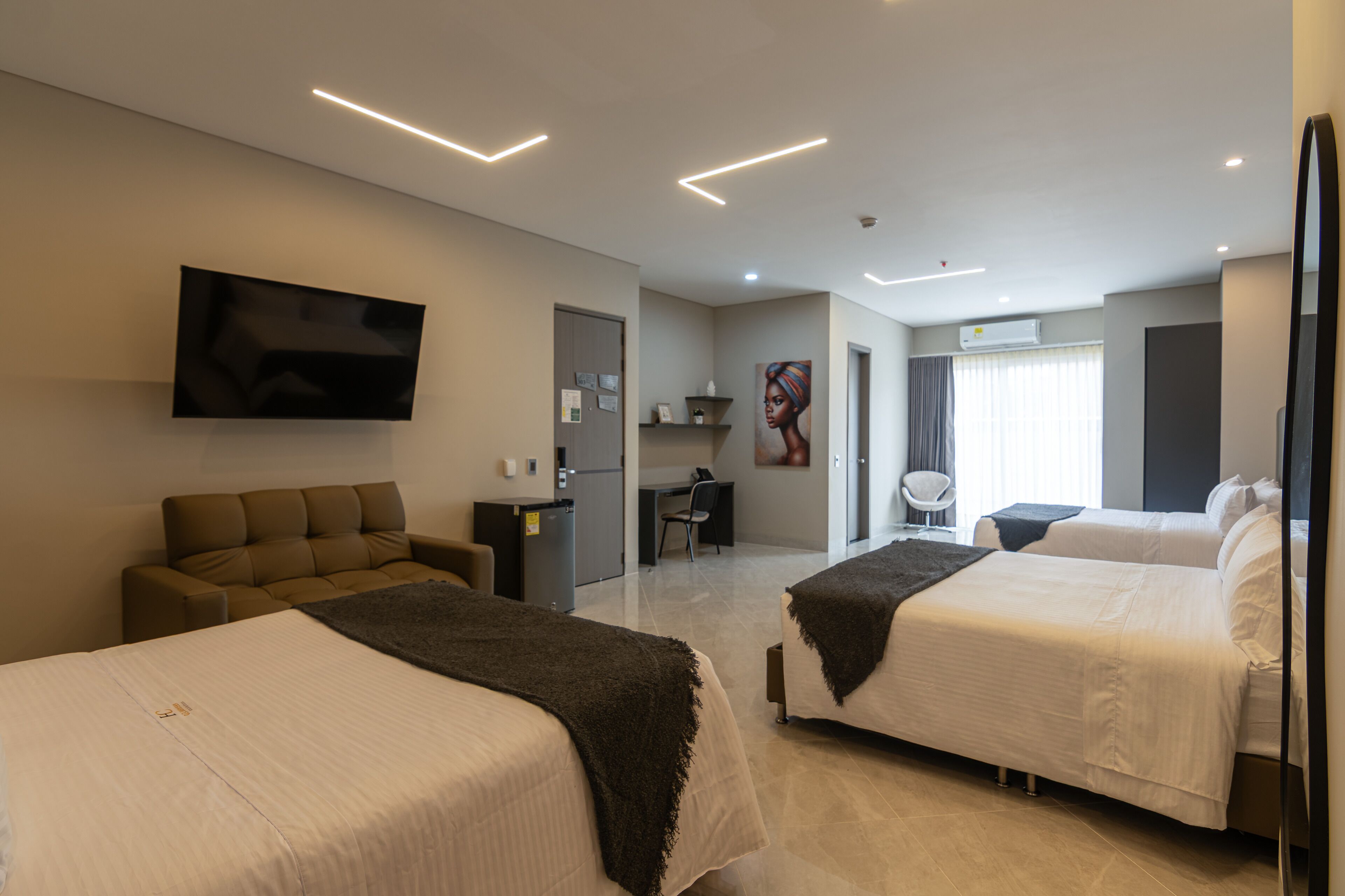 Une chambre d’hôtel avec deux lits, un canapé, un téléviseur à écran plat, un bureau et une chaise.