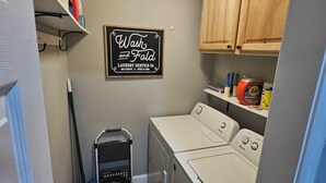 Una sala de lavandería con un letrero que dice 'Wash and Fold Laundry Service Co. Servicio de lavado y doblado, autoservicio y abierto las 24 horas'.