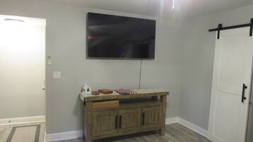 A room with a ceiling fan, a television mounted on the wall, a wooden cabinet with drawers, a patterned rug, and a door with a black handle.