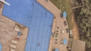 Vista aérea de una zona de piscina con una piscina grande, varias piscinas más pequeñas y un área de estar cubierta.