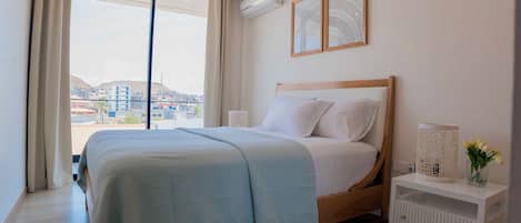 A bedroom with a large bed, a bedside table with a lamp, and a view of the city through the window.