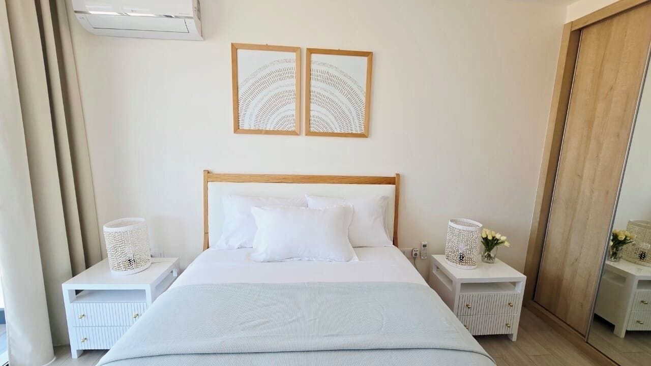 A bedroom with a bed, two nightstands, a mirror, and two framed artworks on the wall.